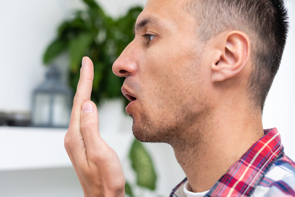 Bad breath. Halitosis concept. Young man checking his breath with his hand.