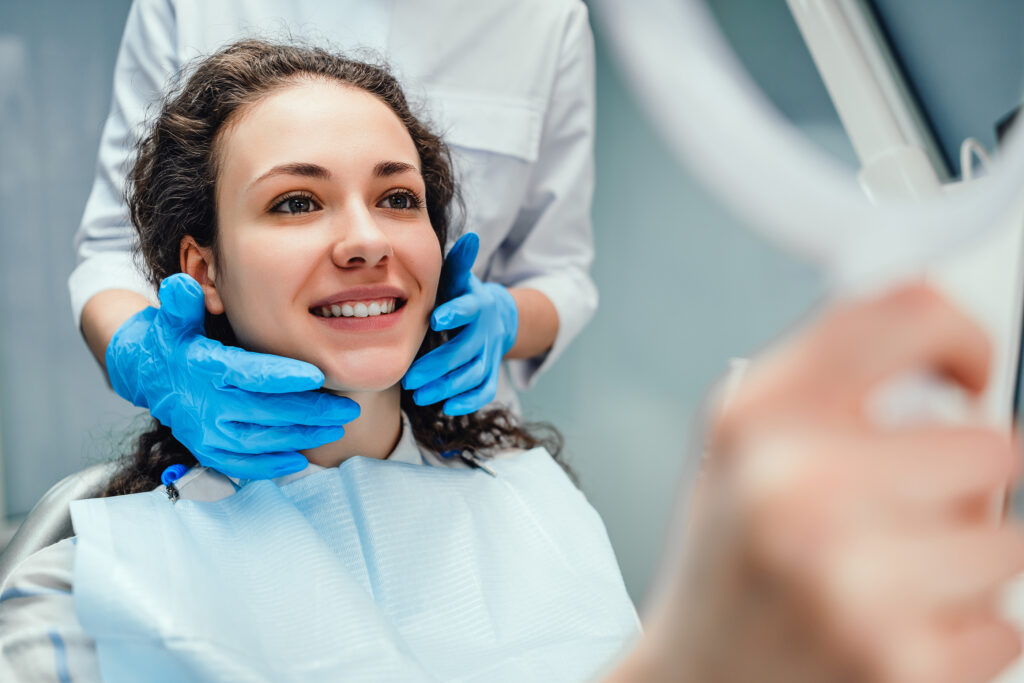 A woman is sitting at a dentist's reception. She looks in the mirror at her teeth. A dentist is sitting next to each other. Woman smiling. Happy patient and dentist concept.
